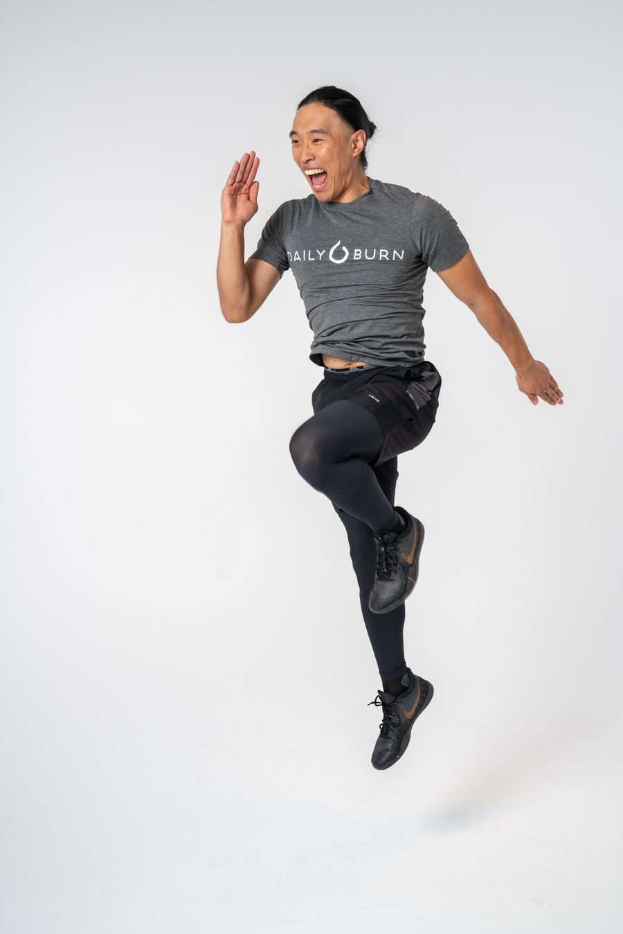 Chris mid-jump laughing in a Daily Burn shirt on set